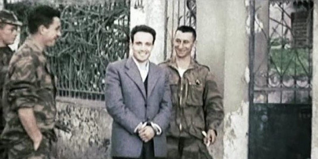Assassinat de Larbi Ben M’hidi : Emmanuel Macron rompt 67 ans de silence et reconnaît le crime d’État Deux hommes en costume et uniforme se serrent la main devant une grille en fer forgé.