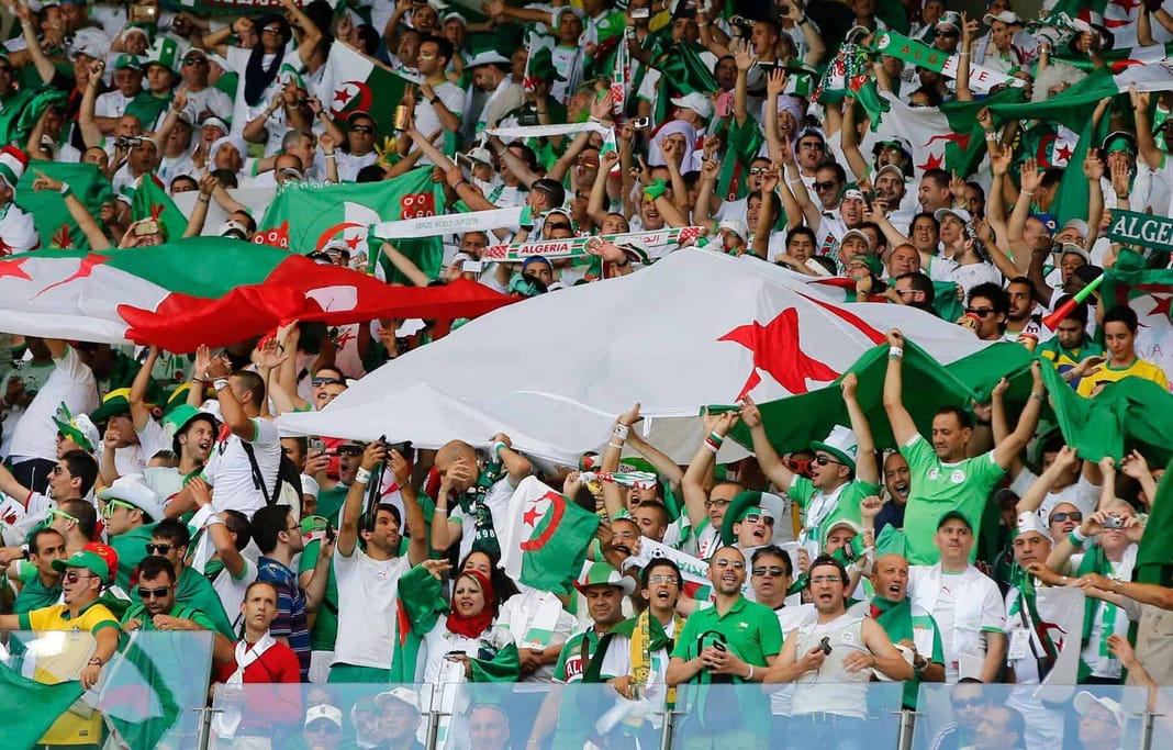 Supporters algériens avec drapeaux et banderoles lors d'un match.