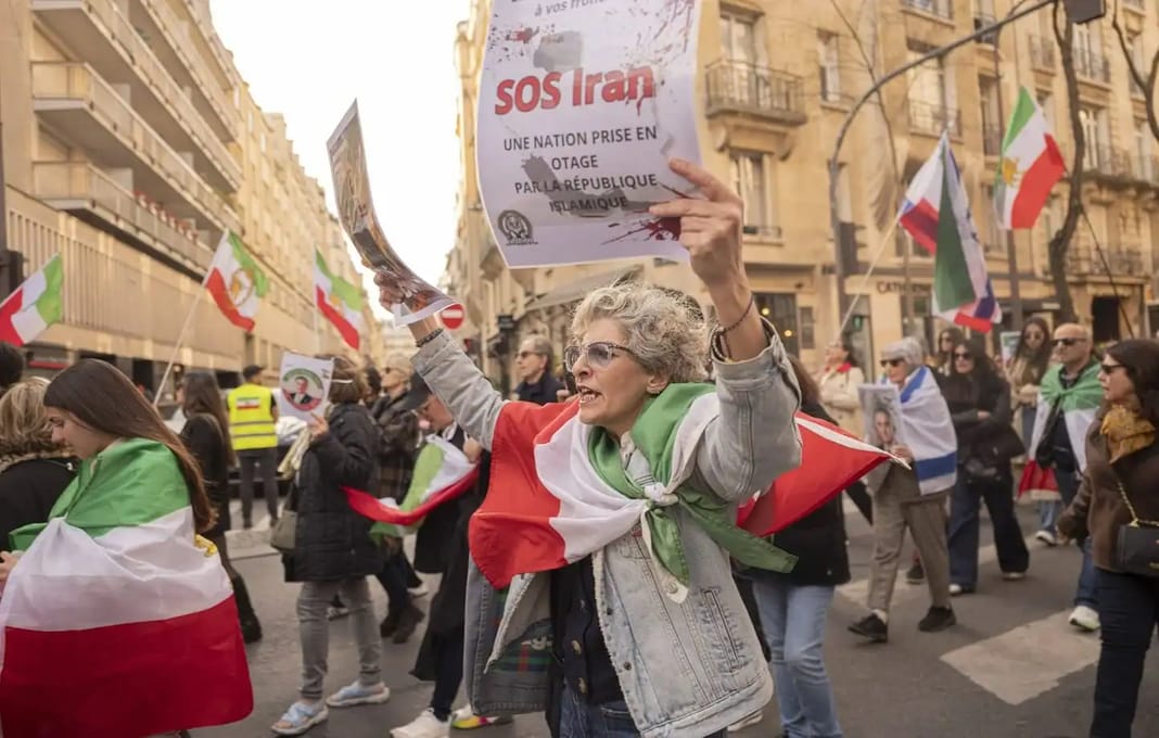 Iran : Trump promet la pire offensive économique jamais menée Femme manifestant avec drapeau algérien et panneau SOS Trap.