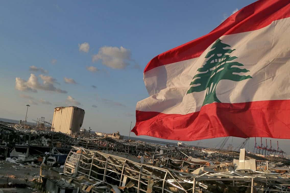 Drapeau du Liban flottant dans un paysage urbain dévasté.