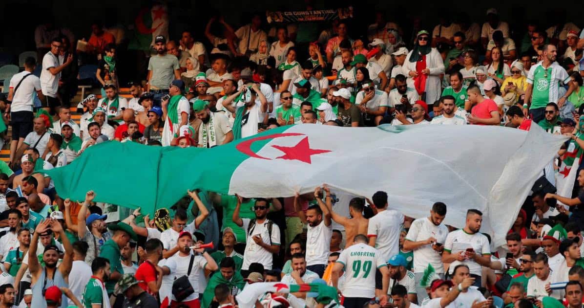 Foule de supporters algériens avec drapeau national lors d'un événement sportif.