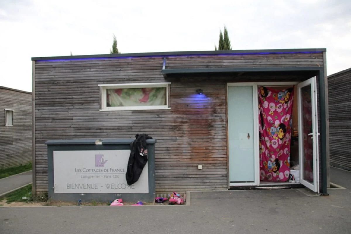 Petite maison en bois avec porte ouverte et rideau coloré à l'intérieur.