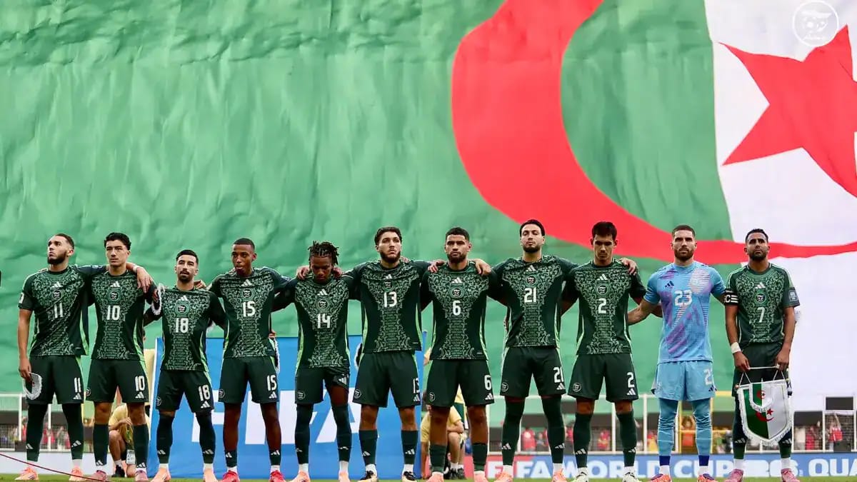 Les joueurs de l'équipe d'Algérie alignés devant un drapeau national.