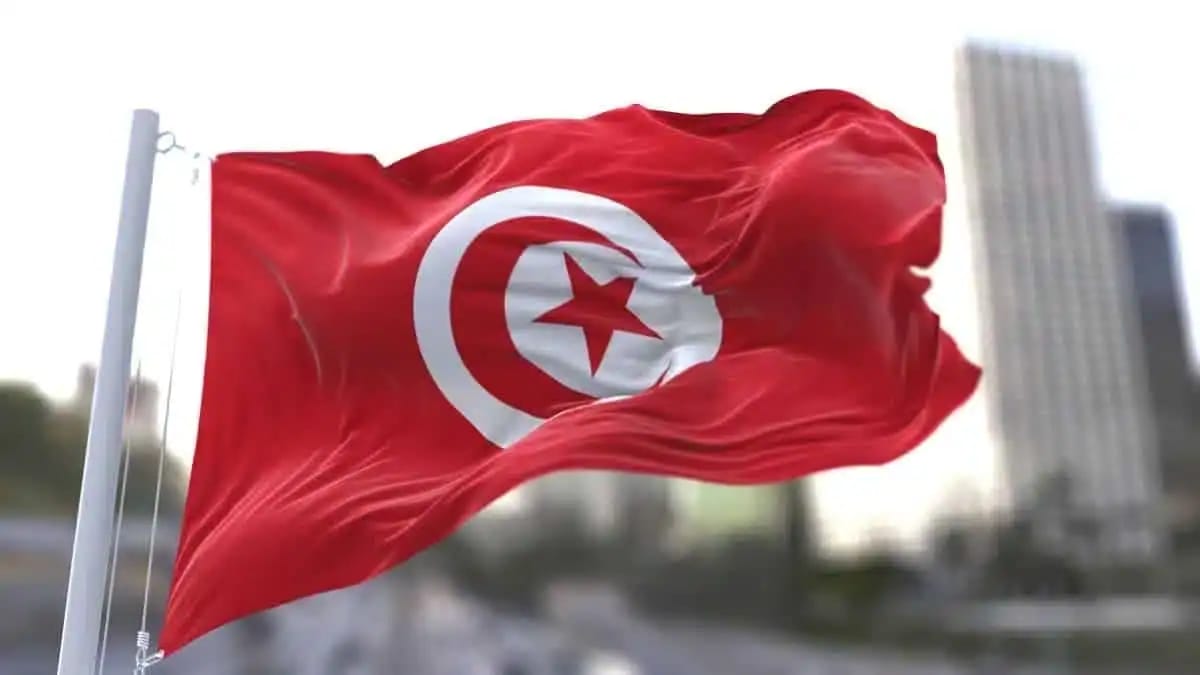 Drapeau tunisien flottant dans le vent avec bâtiments en arrière-plan.