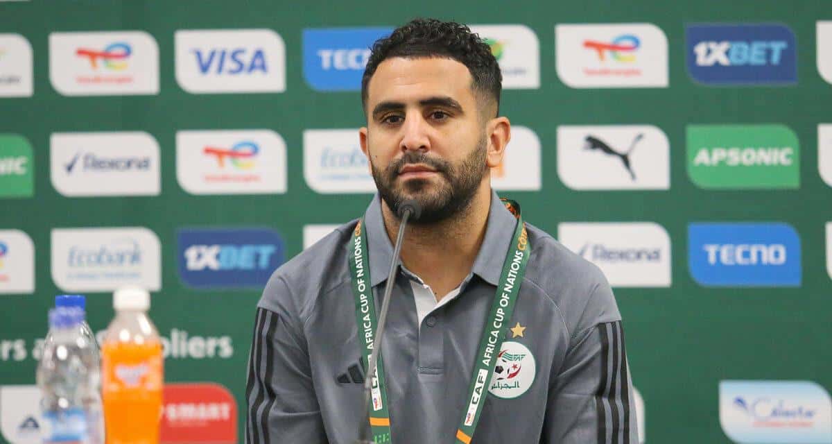 Riyad Mahrez en conférence, portant un badge et une veste grise.