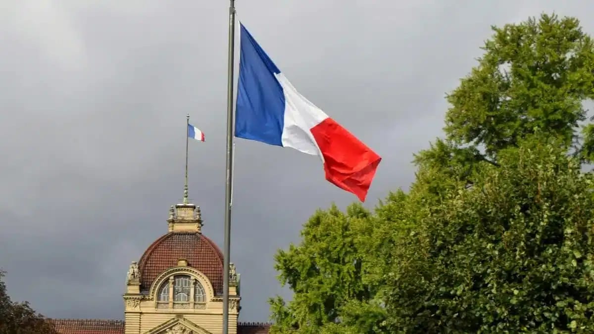 Drapeau français sur un mât avec ciel nuageux en arrière-plan.