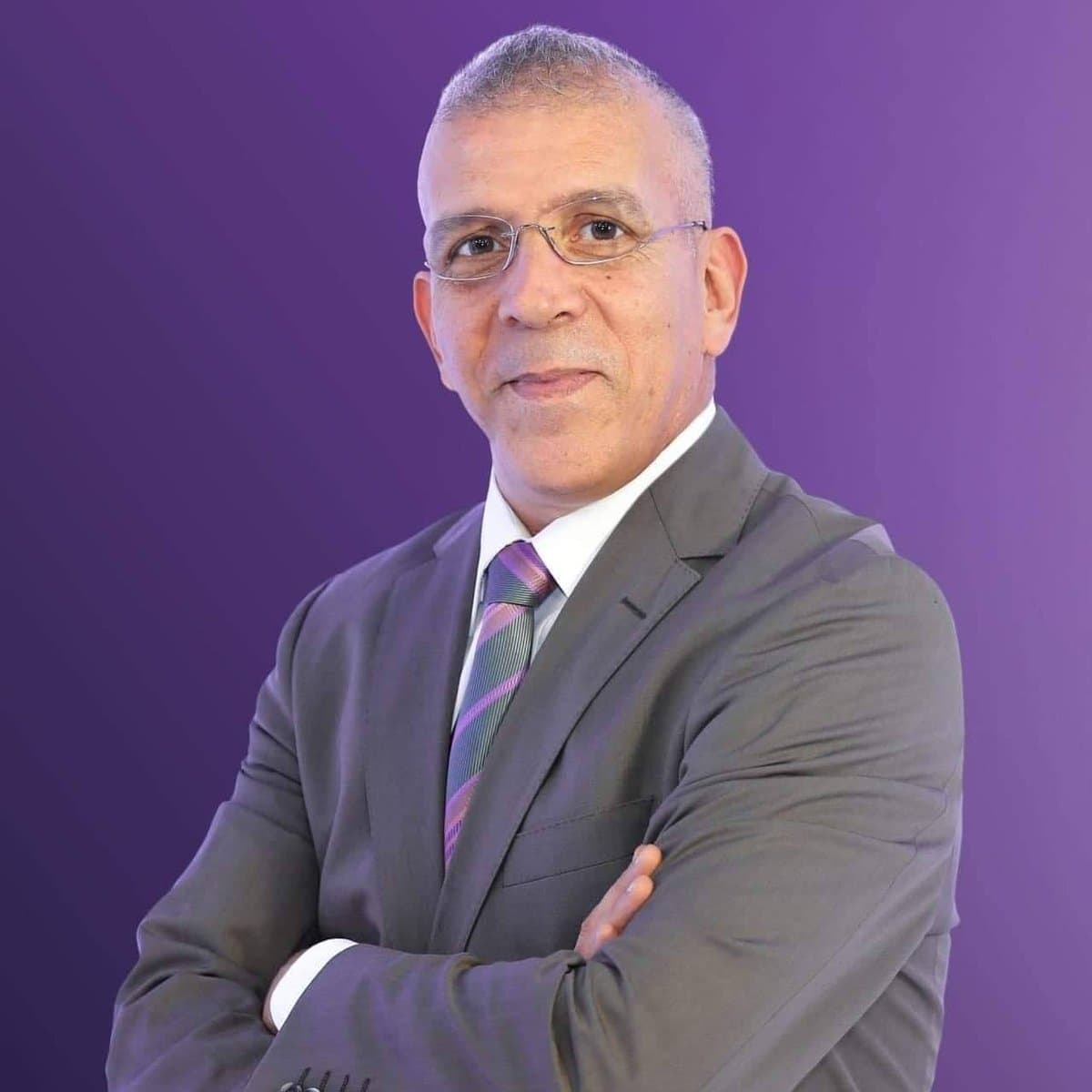 Hafid Derradji en costume avec fond violet.
