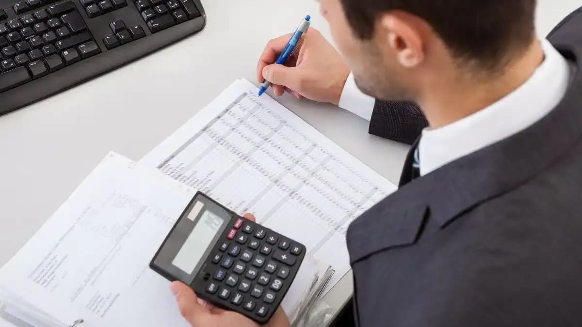 Homme d'affaires utilisant une calculatrice et des documents financiers.