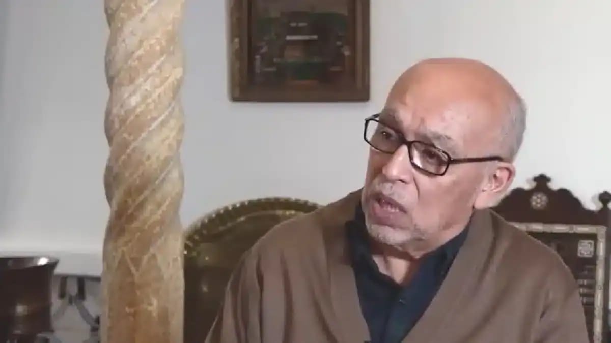 Homme âgé parlant, lunettes, intérieur classique, contexte historique.