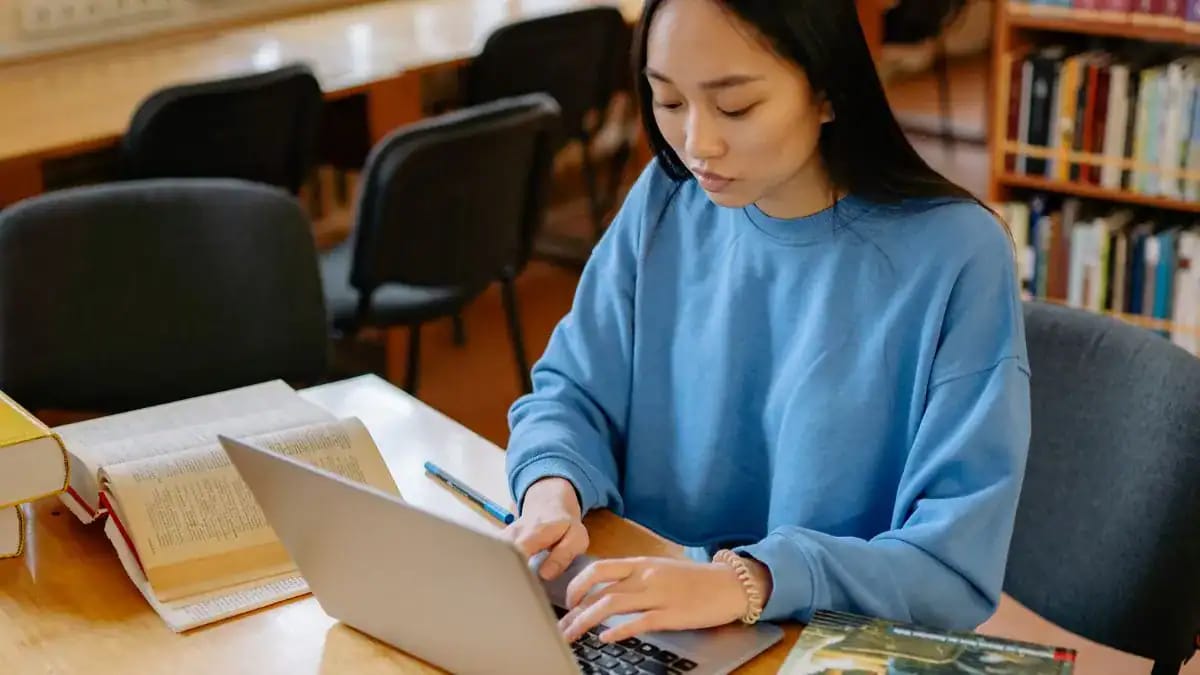 Jeune femme étudiant à la bibliothèque avec ordinateur et livres.