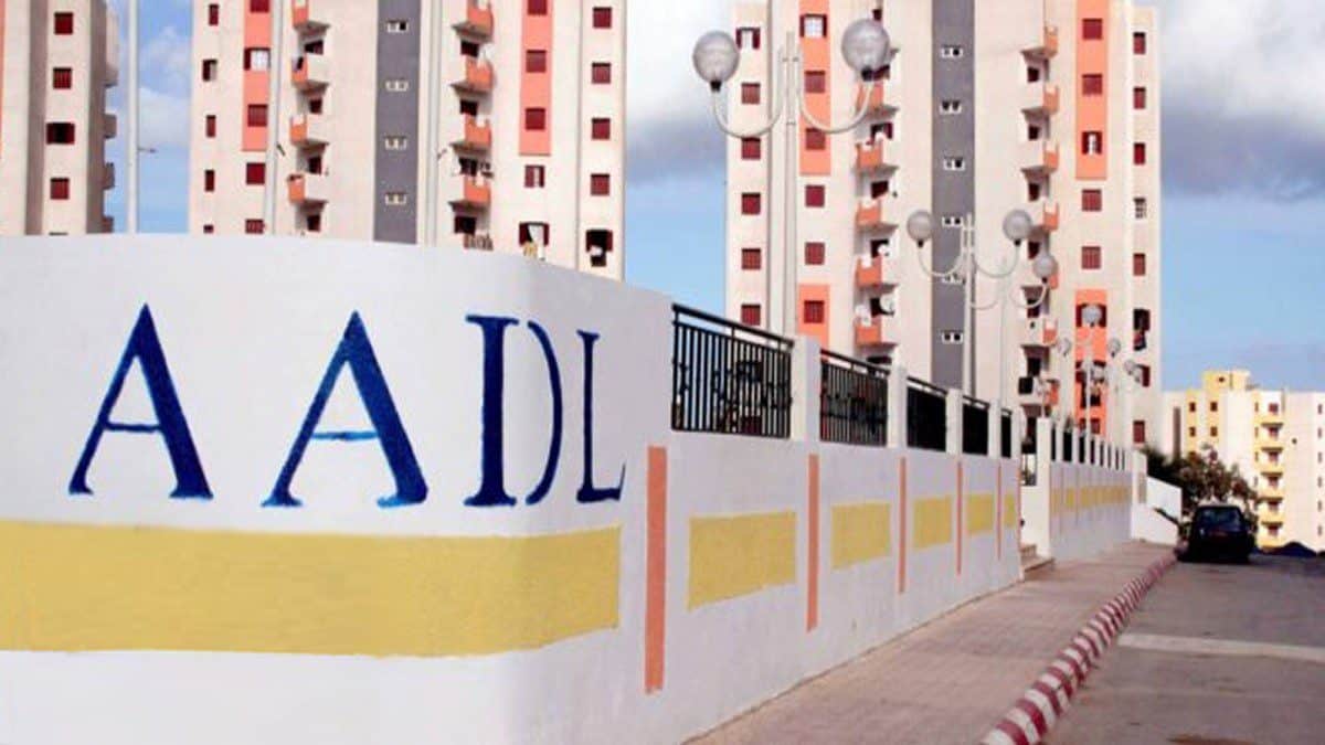 Mur de livraison AADL 3 avec logo visible, bâtiments en arrière-plan.