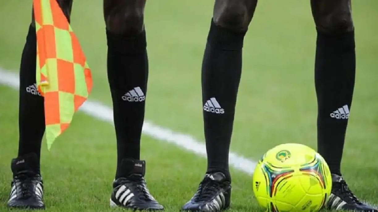 Arbitres de football avec ballon et drapeau sur le terrain.