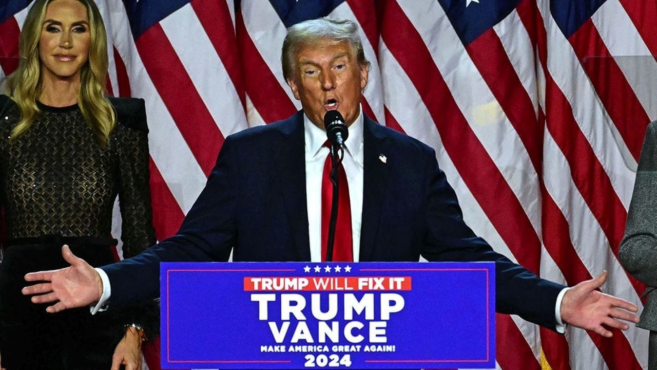 Donald Trump parlant à un événement avec drapeaux américains en arrière-plan.