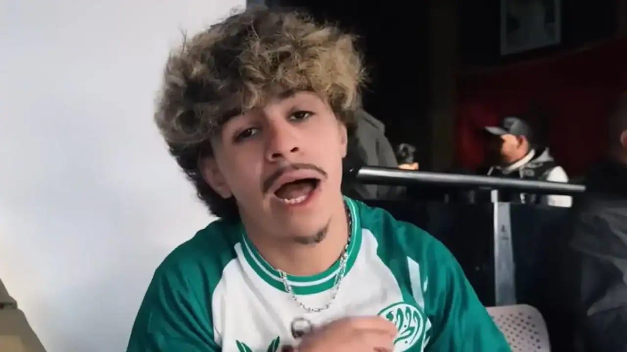 Jeune homme parlant avec expression expressive, cheveux bouclés, en intérieur.