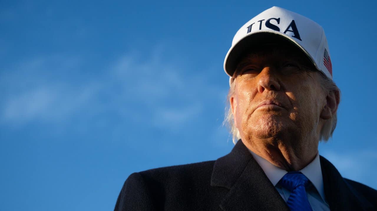 Donald Trump portant une casquette "USA" contre un ciel bleu.
