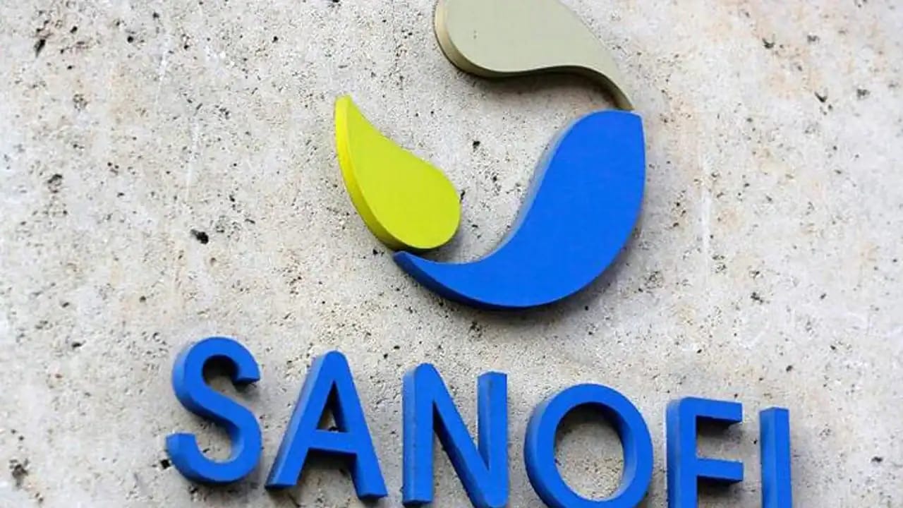 Logo de Sanofi avec couleurs bleu, vert et gris sur mur en béton.
