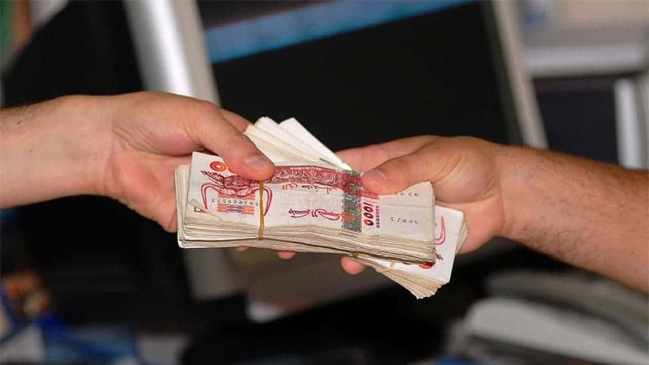 Deux mains échangeant de l'argent en billets de banque algériens.