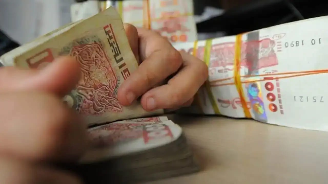 Main manipulant des billets de banque algériens en rouleaux.