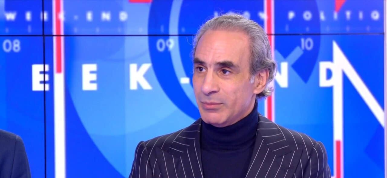 Homme en costume à l'écran de télévision avec logo bleu.