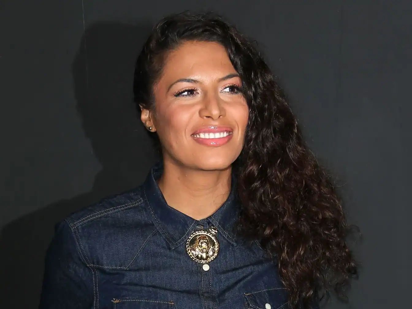 Zaho souriante avec cheveux bouclés, vêtue d'une veste en denim.