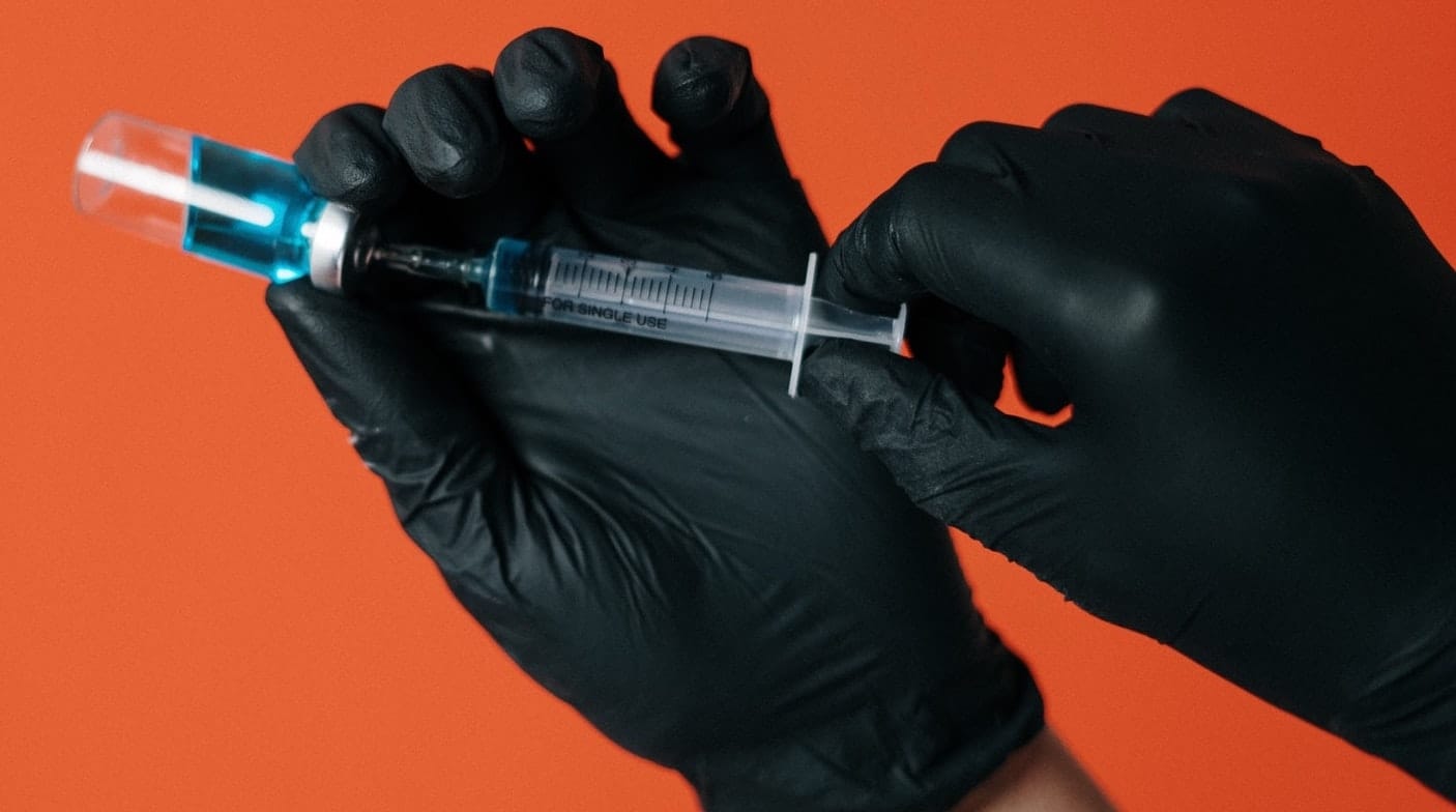 Main en gants noirs avec une seringue prête à être injectée.