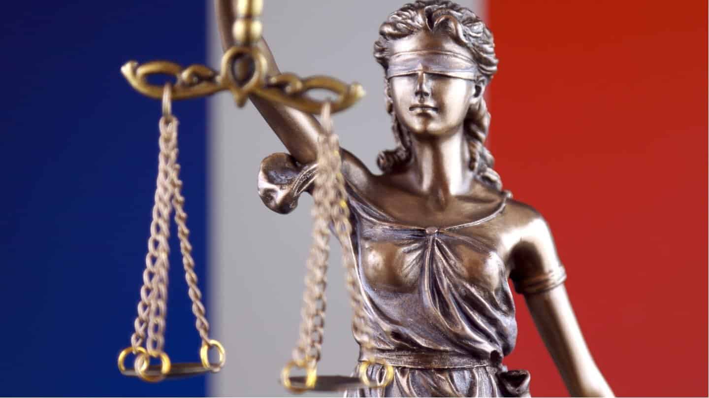 Statue de la justice avec drapeau français en arrière-plan.
