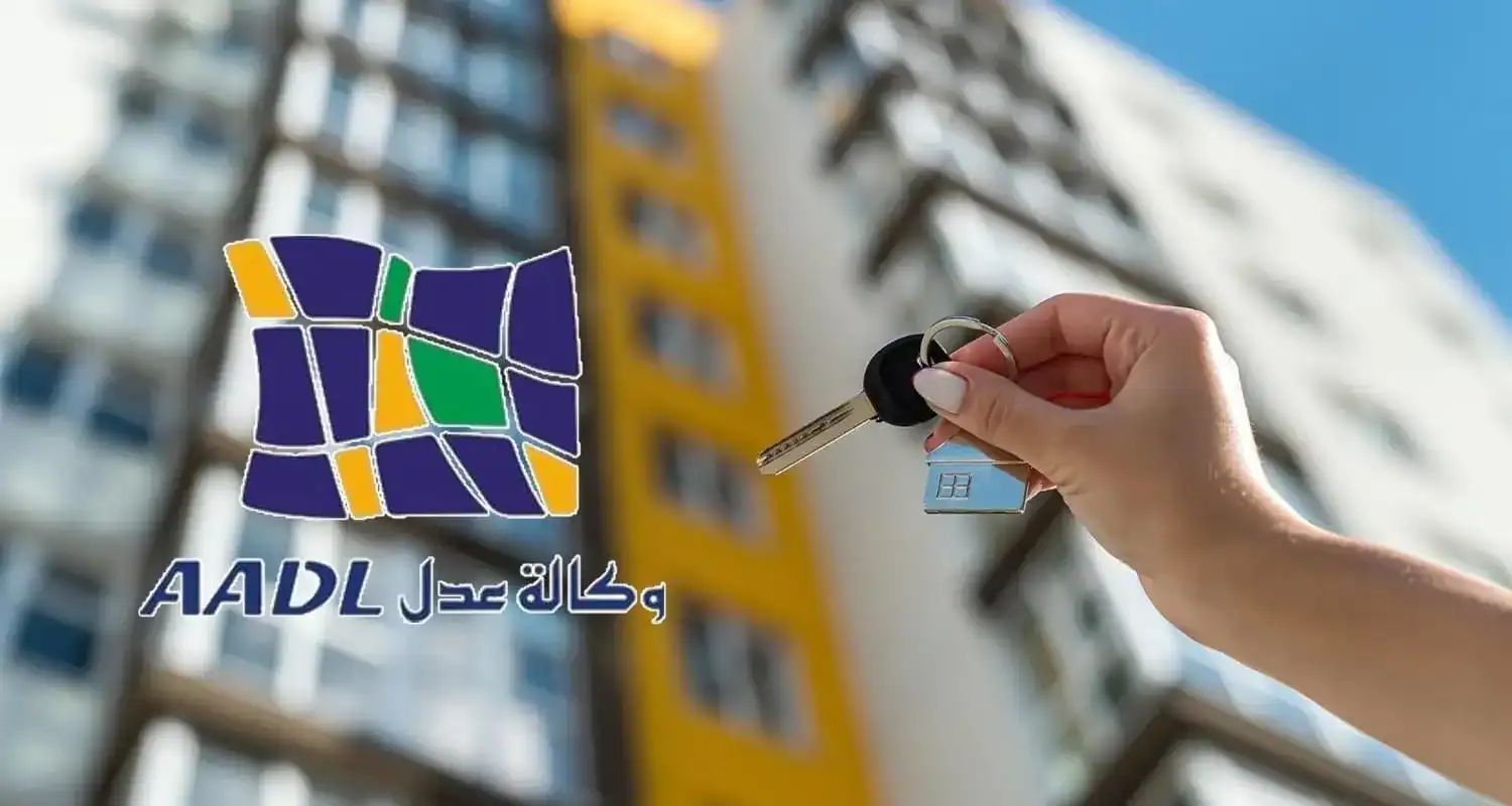 Clé de logement AADL devant un immeuble résidentiel en construction.