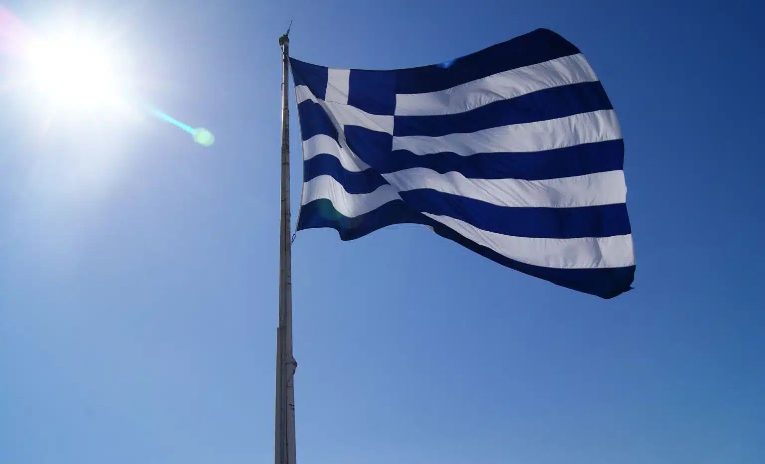 Drapeau grec flottant sous un ciel ensoleillé.