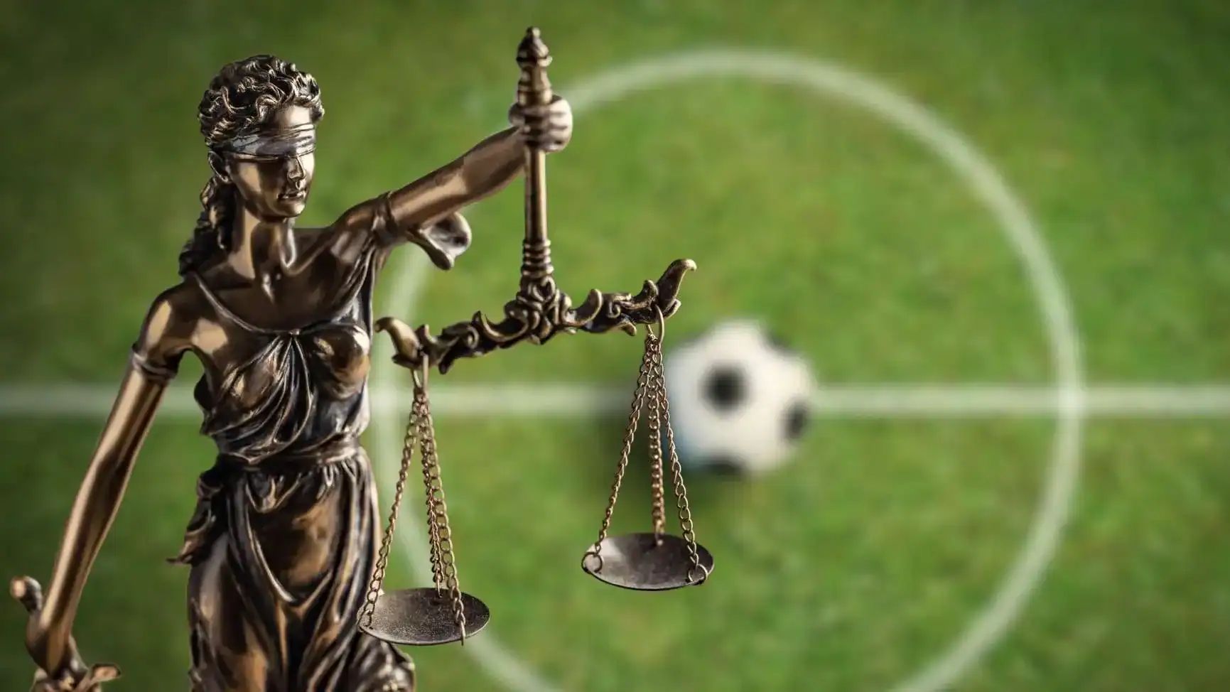Statue de la justice avec un ballon de football en arrière-plan.