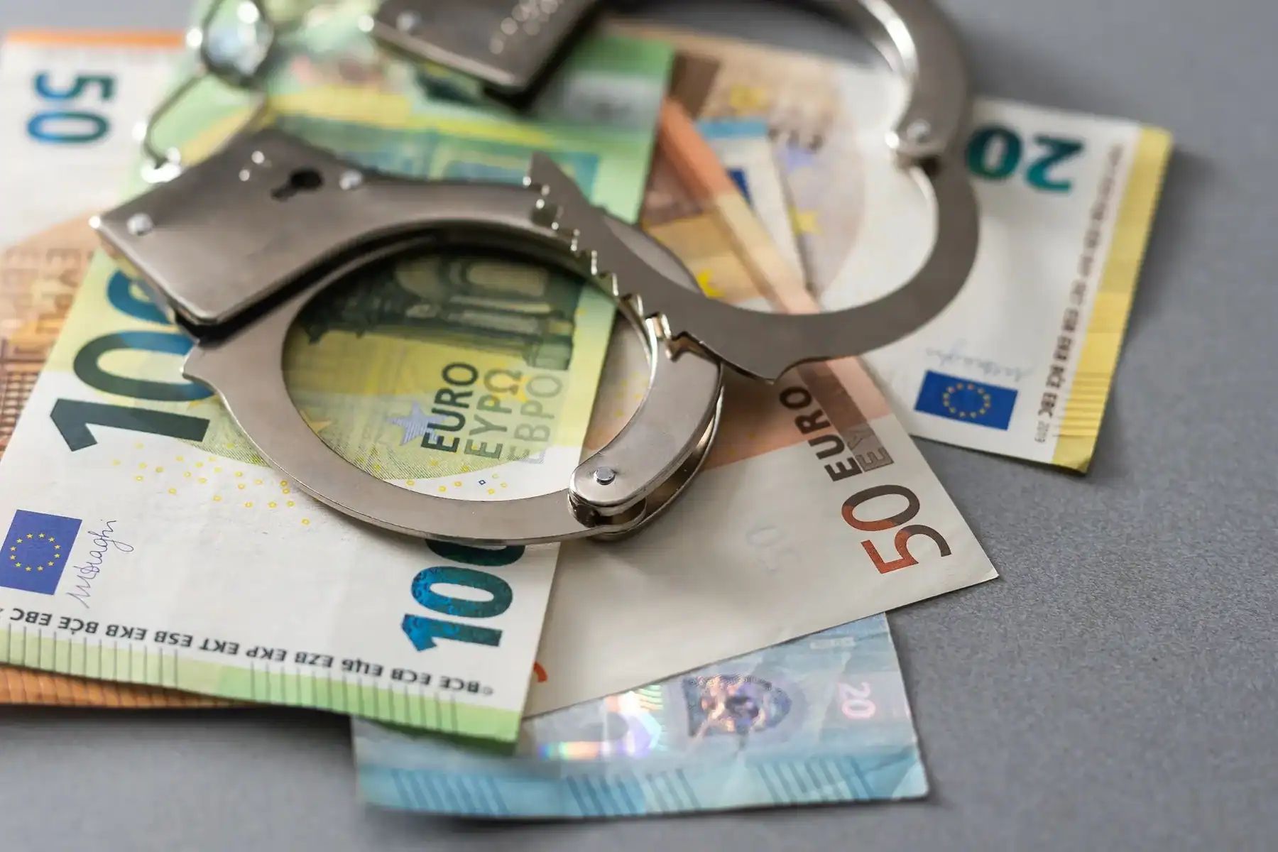 Menottes sur des billets de banque euro, illustrant la fraude financière.