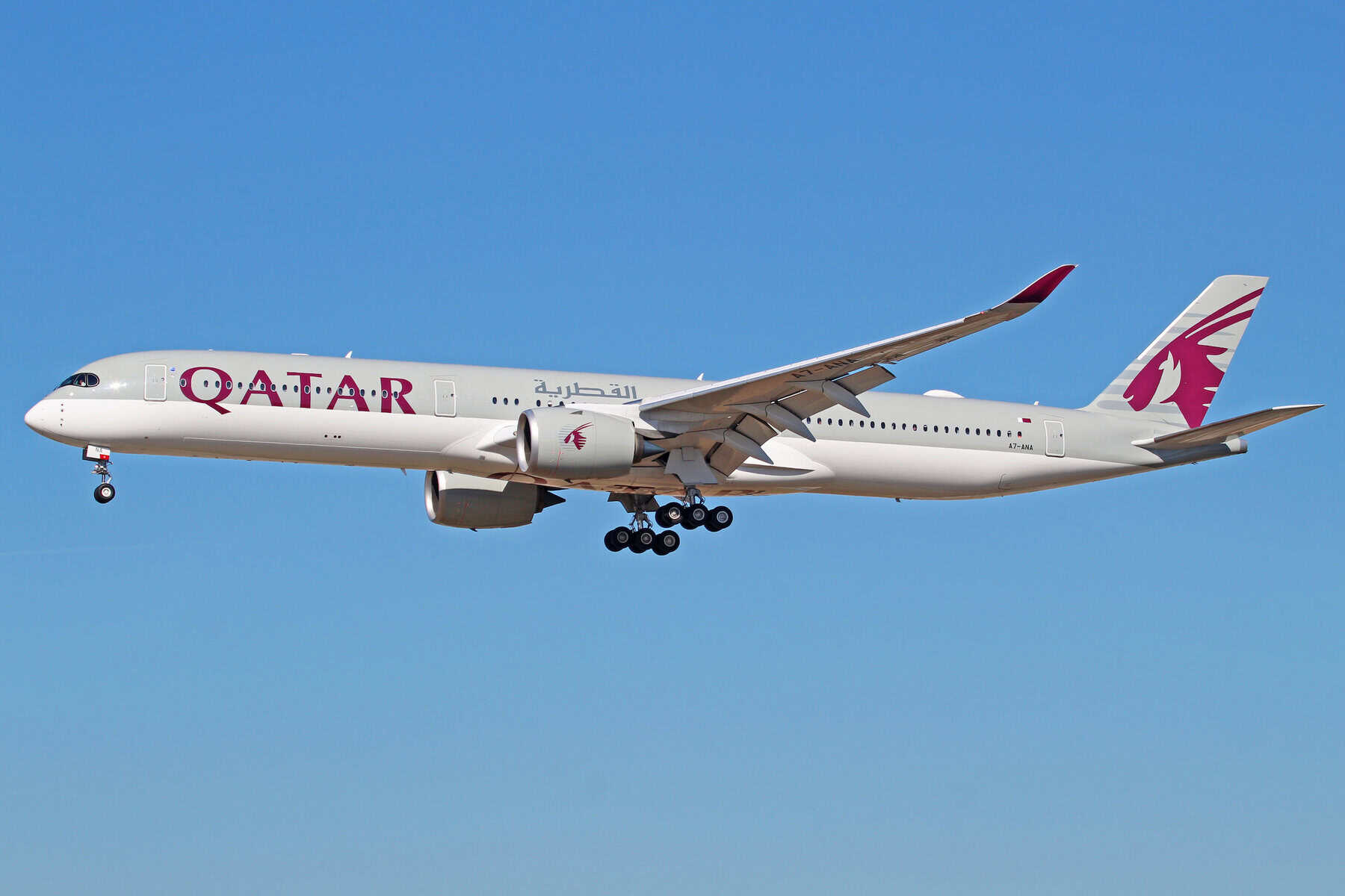 Avion Qatar Airways en vol avec logo visible contre ciel bleu clair.