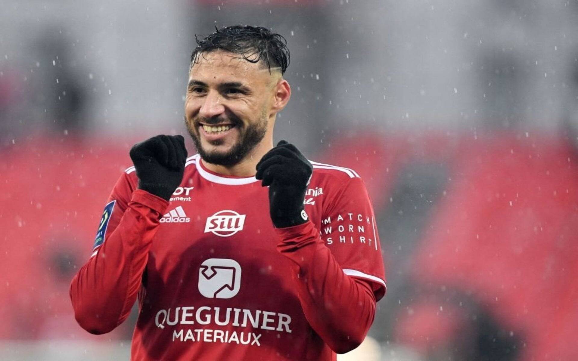 Youcef Belaili souriant en tenue de football sous la pluie.