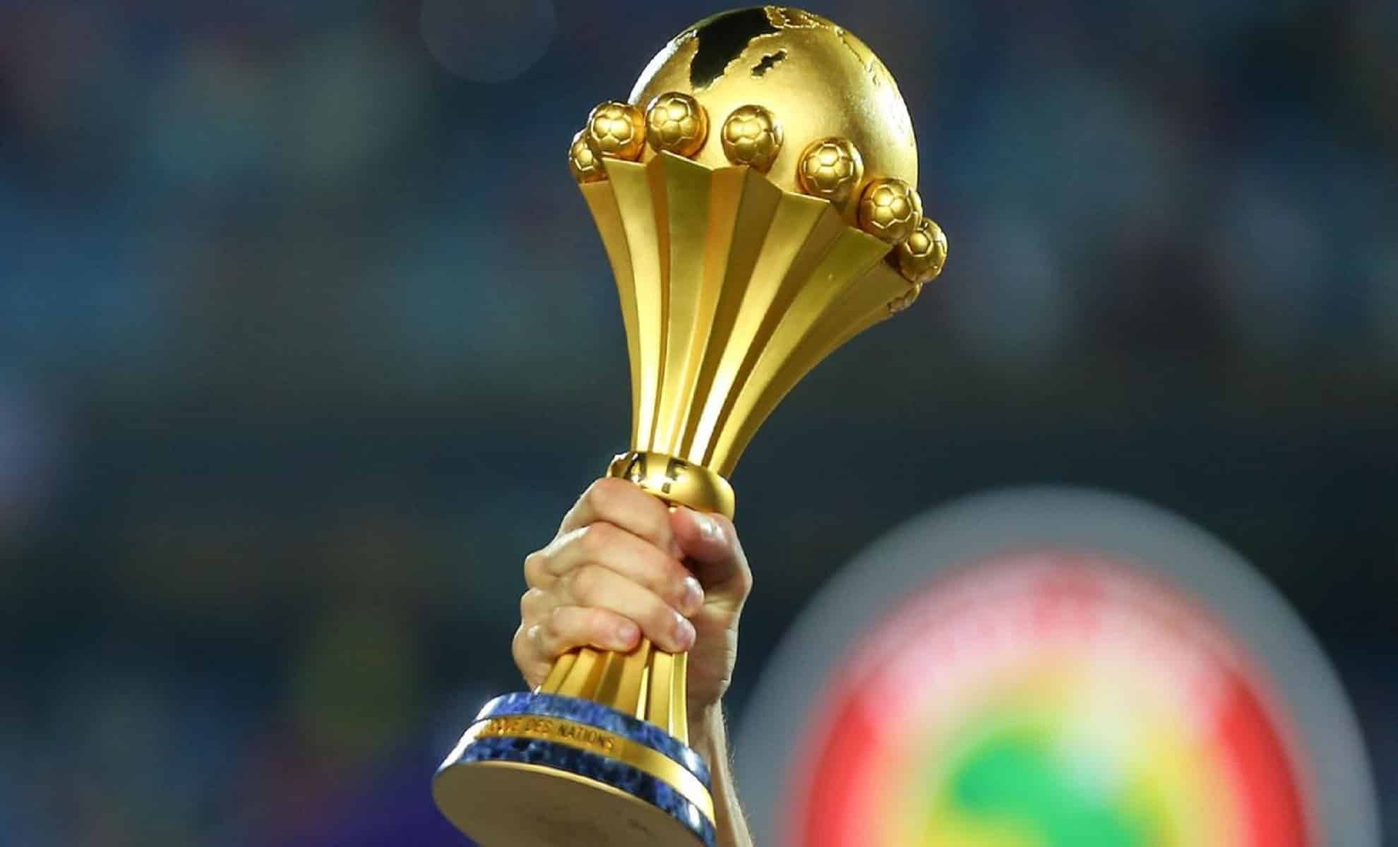 Trophée de la CAN 2025 en or brillant dans une main.