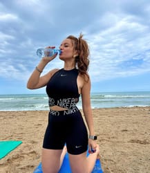 Femme sportive buvant de l'eau sur la plage par temps nuageux.