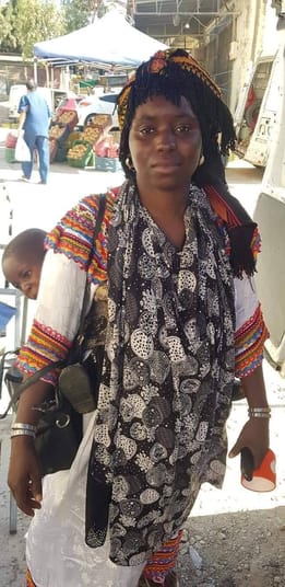 Femme migrante portant une robe kabyle traditionnelle dans un marché.