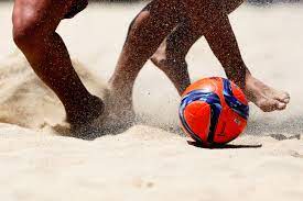 Joueurs de beach soccer en action sur la plage avec un ballon coloré.
