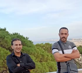 Deux hommes posant devant un paysage naturel avec ville en arrière-plan.