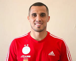 Mustapha Zeghba portant maillot rouge de football, souriant.