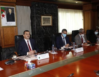 Groupe de personnes en réunion officielle, portant des masques, dans une salle de conférence.