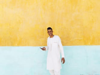 Jeune homme souriant avec smartphone devant mur jaune et bleu.