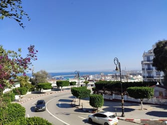 Vue sur la ville, la mer et le ciel bleu avec des arbres et des lampadaires.