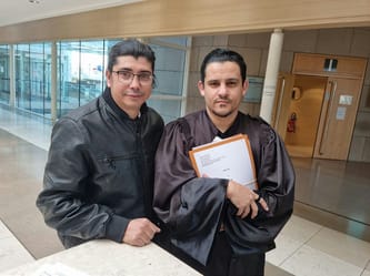 Deux hommes posant, un en robe de graduation, dans un bâtiment moderne.