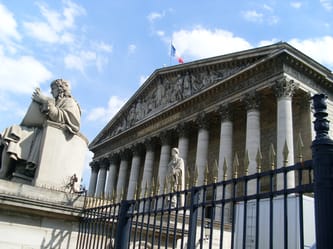 Vue de l'Assemblée nationale avec statues et drapeau français.