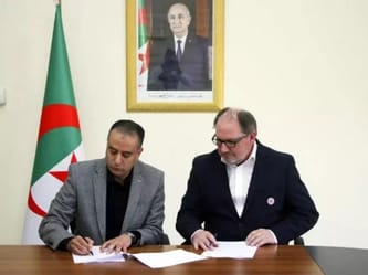 Deux hommes signent un document lors d'une réunion officielle.