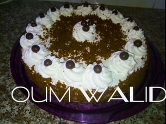 Gâteau rond décoré de crème, chocolat et cerises noires pour célébration.