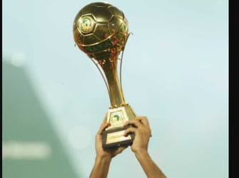 Main levant un trophée de football en or avec un ballon doré.