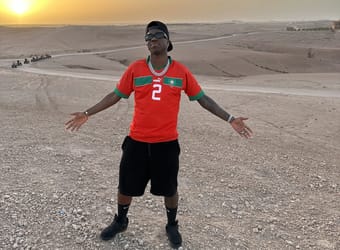 Jeune homme portant un maillot de football dans un désert au coucher du soleil.