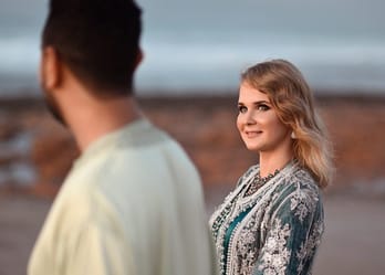 Jeune femme souriante regardant un homme sur la plage au coucher du soleil.