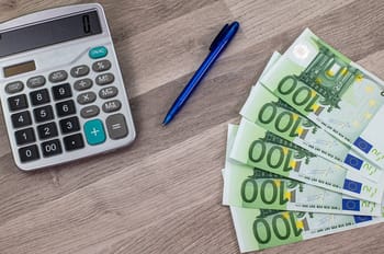 Calculatrice et billets de 100 euros sur une table en bois.