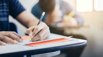 Étudiant écrivant sur un cahier dans une salle de classe lumineuse.